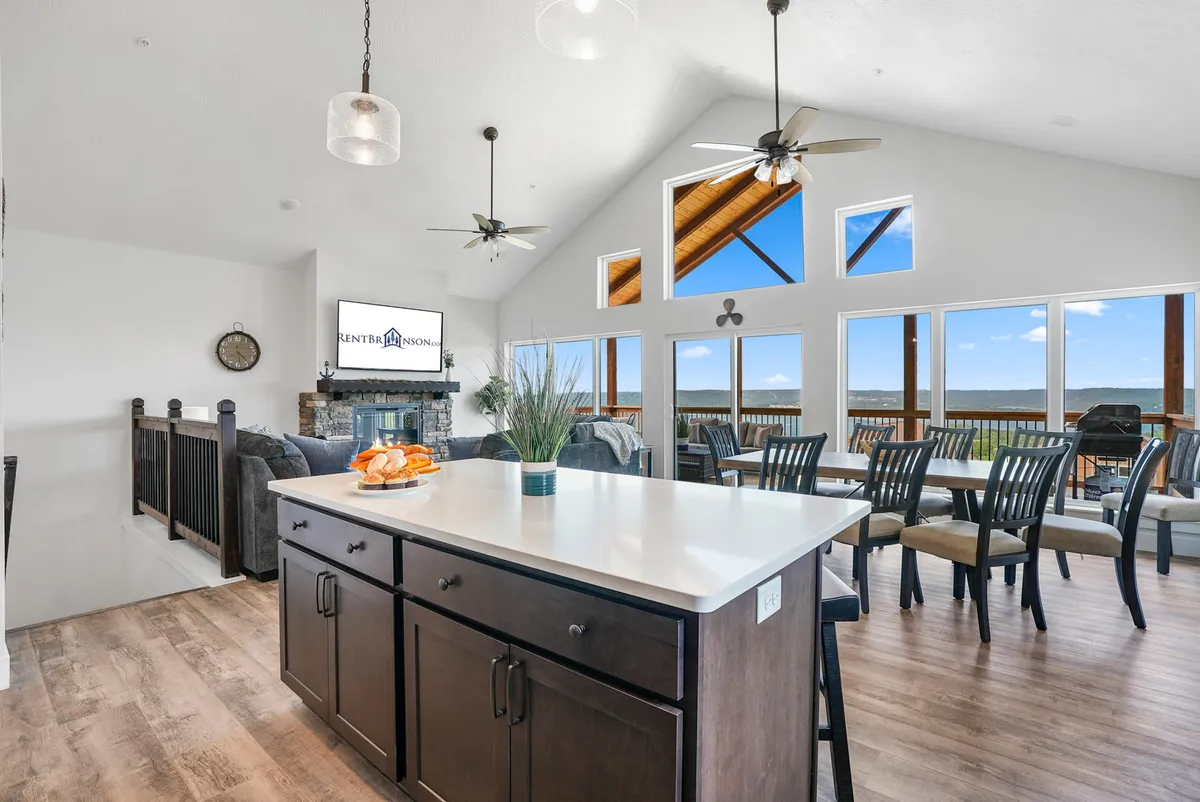 This image showcases a spacious kitchen with a large island, modern cabinetry, and expansive windows. The dining area is visible, offering a seamless flow between cooking and gathering spaces. Ample natural light highlights the inviting atmosphere.