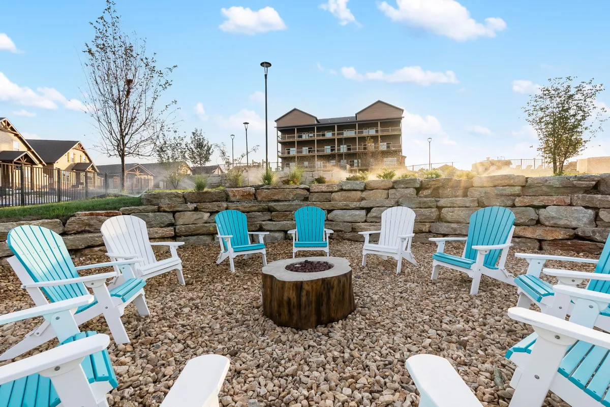 A cozy fire pit scene with Adirondack chairs arranged around a glowing fire, set against a tranquil backdrop. The area looks ideal for evening gatherings, storytelling, and roasting s’mores as the sun sets.