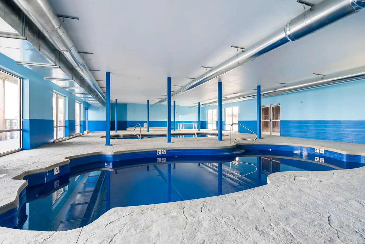 An inviting indoor pool space with blue walls, abundant windows, and a calm, relaxing atmosphere. The pool is ready for guests regardless of season or weather, providing year-round aquatic enjoyment.