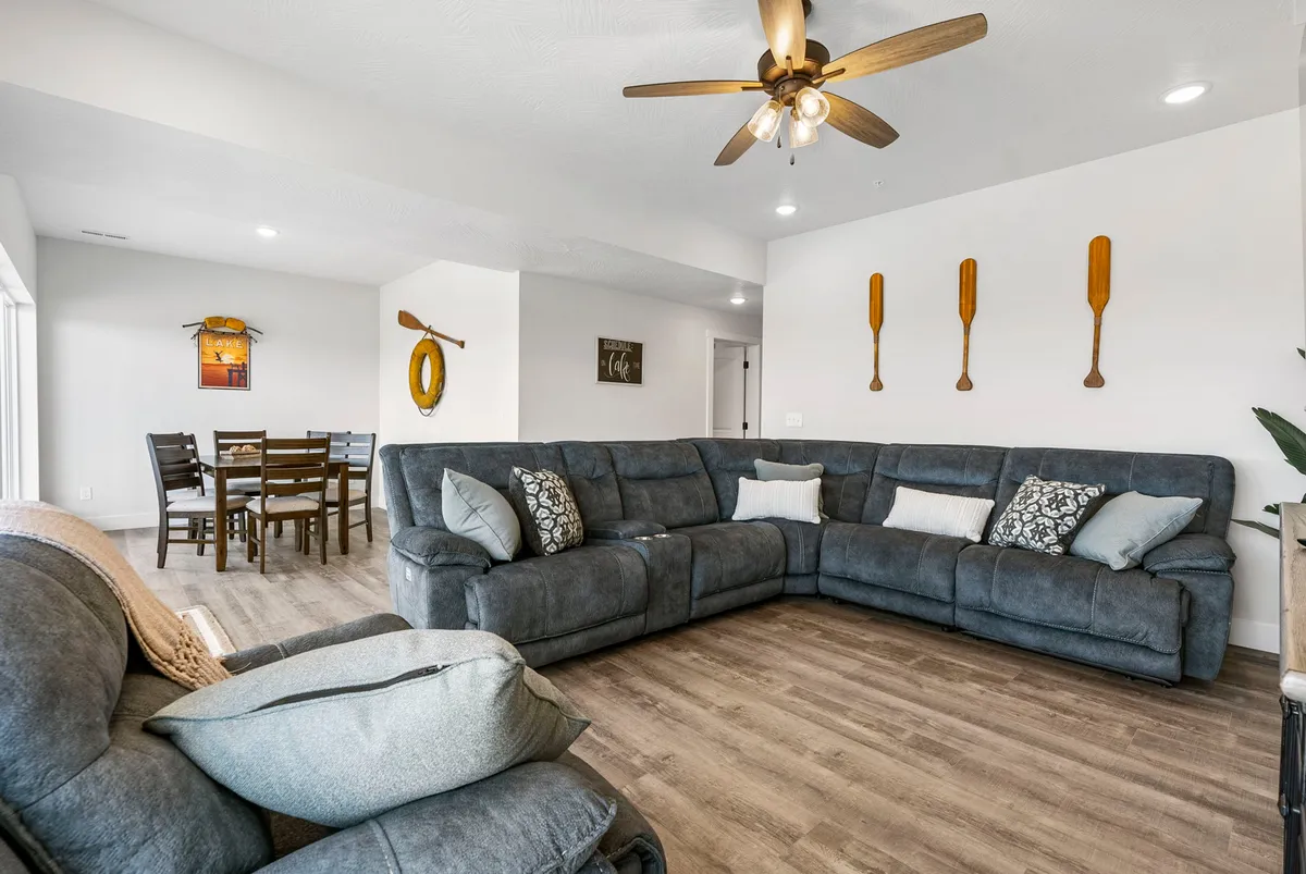 A large sectional sofa anchors a cozy living/lounge area, with a dining table nearby and decorative paddles on the wall, evoking a lakeside retreat. The space is open, comfortable, and ideal for both group relaxation and meals.
