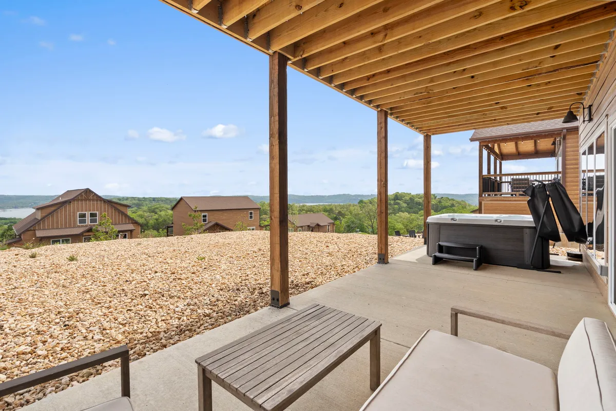 This image showcases an inviting outdoor hot tub set on a wooden patio with sturdy beams, overlooking the scenic hills of the Ozarks. The tranquil setting features plenty of open space and natural surroundings, emphasizing relaxation and the connection to nature.