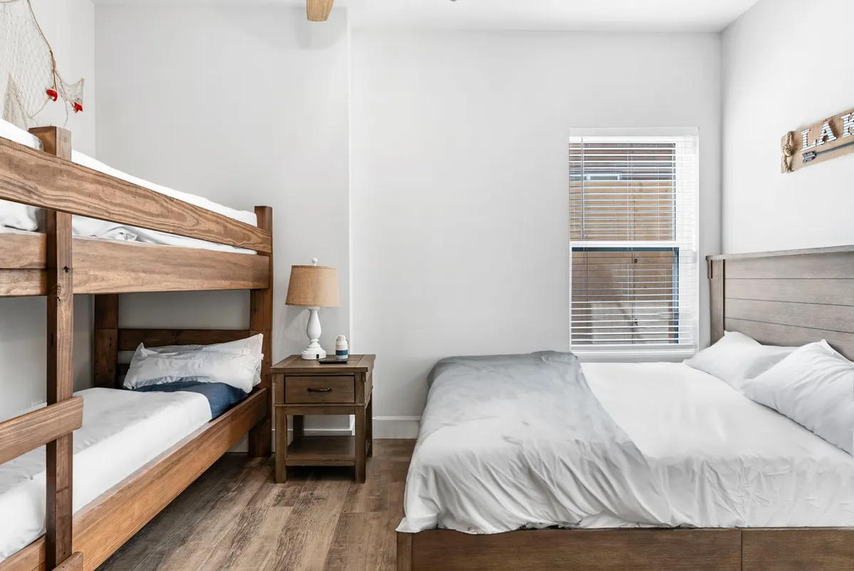 A family-friendly bedroom setup with a queen bed and a twin-over-twin bunk bed. The space includes a nightstand, lamp, and a window, making it ideal for kids or young families seeking both comfort and convenience.