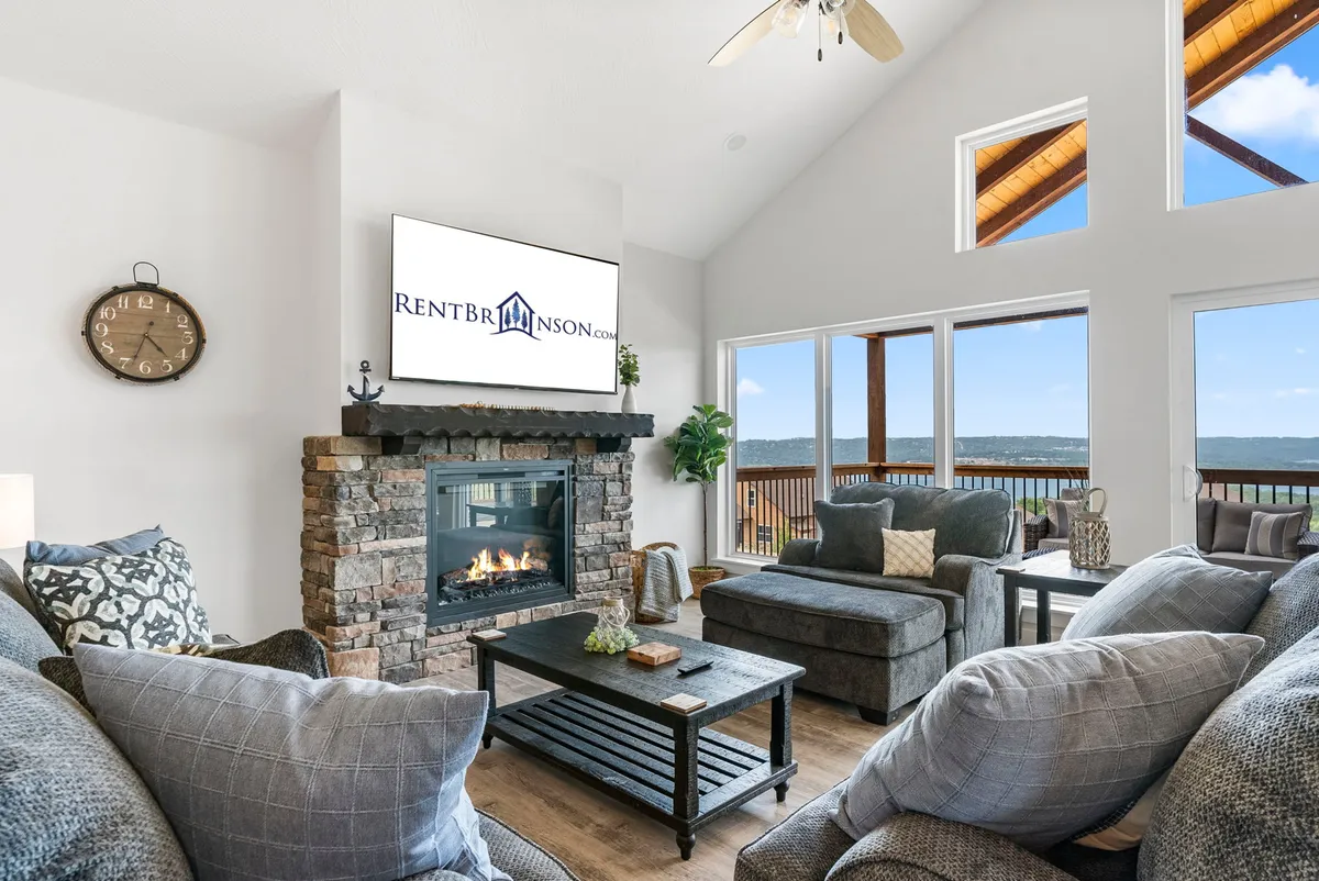 A cozy lounge area with a fireplace, large windows framing lake views, and comfortable seating arranged for conversation or movie nights. The space feels warm and inviting, ideal for group relaxation.