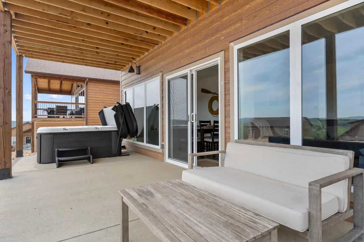 A tranquil, private patio with an outdoor seating area, a large hot tub, and glass doors leading back inside. The setting is ideal for soaking in the hot tub under the stars or gathering outdoors for peaceful conversation.