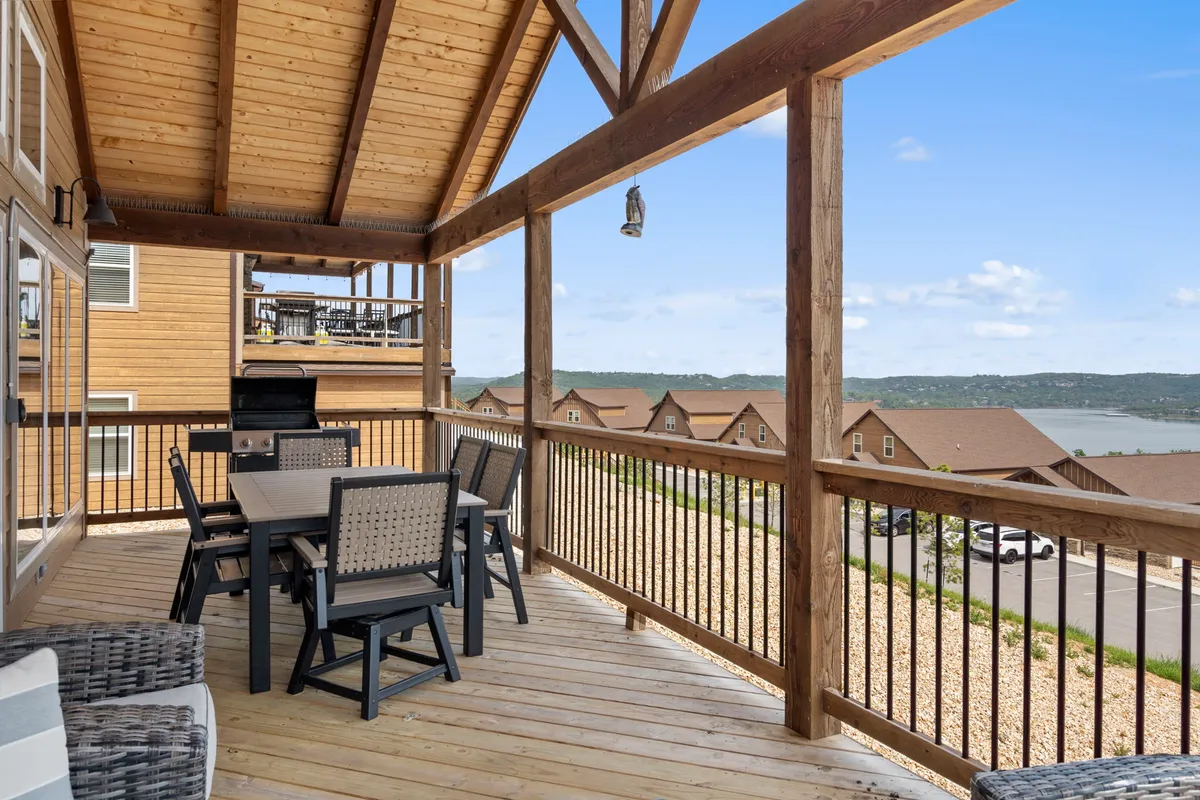 An exterior shot of a wooden deck featuring a dining table, grill, and panoramic lake views. The layout offers ample space for outdoor dining, barbecuing, and relaxing, all with the lake as a beautiful backdrop.